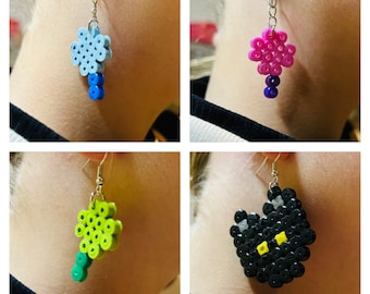 May include: Four pairs of beaded earrings. The earrings are made of colorful plastic beads and are shaped like flowers, a cat, and a heart. The earrings are hanging from silver hooks.