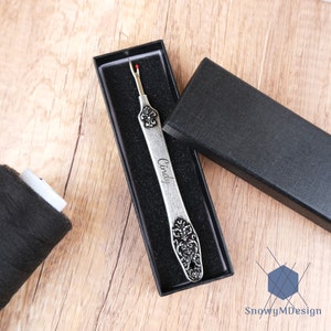 May include: A silver thread snipper with an ornate design and the name "Cindy" engraved on it. The snipper is in a black velvet box.