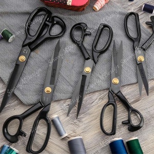 May include: Five black fabric shears with gold accents and the word "Barry" engraved on the blades. The shears are arranged on a gray and brown fabric surface.
