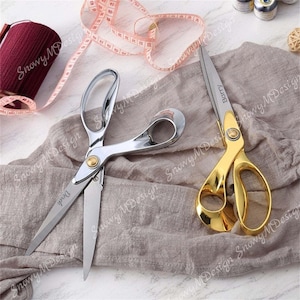 May include: Two pairs of fabric shears with silver and gold handles. The silver shears are labeled "Derek" and the gold shears are labeled "Barry".