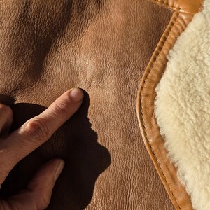 Close-up of button closure, lower buttons intact, faint mark where top button missing, natural sheepskin texture.