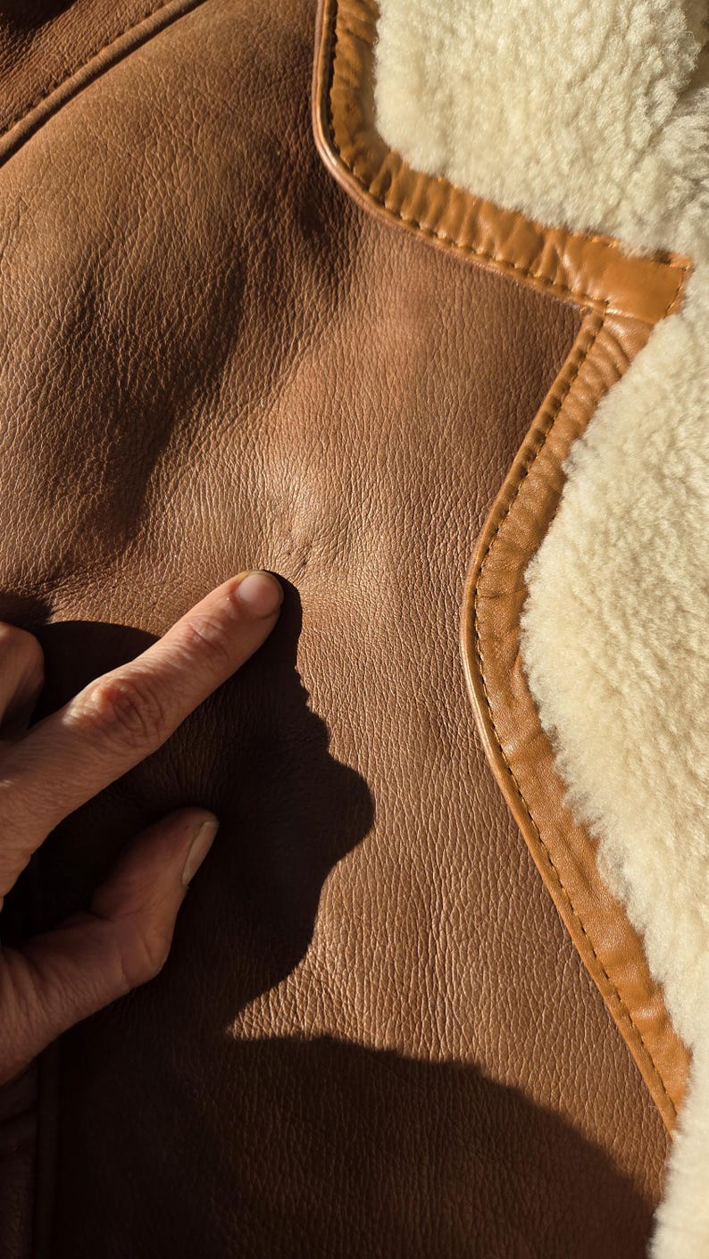 Close-up of button closure, lower buttons intact, faint mark where top button missing, natural sheepskin texture.