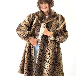 Puede incluir: Un abrigo de piel sintética hasta la rodilla con mangas largas, estampado de leopardo en tonos marrón y negro, cuello ancho y mangas amplias. El abrigo se combina con orejeras de piel sintética a juego, una camiseta blanca y vaqueros azul claro.