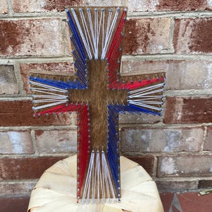 May include: A wooden cross with red, white, and blue string wrapped around it in a starburst pattern.