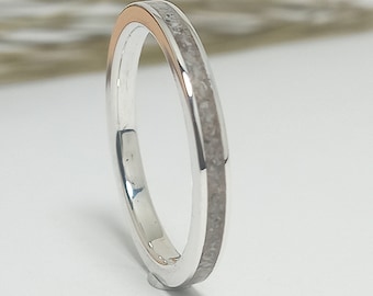 May include: A silver ring with a thin band of rose gold and a white inlay. The inlay is made of crushed stone or sand.