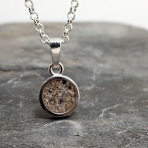 Könnte beinhalten: Eine silberne Kettenkette mit einem runden Anhänger, der Sand enthält. Der Anhänger hat einen Durchmesser von etwa 2,5 cm.