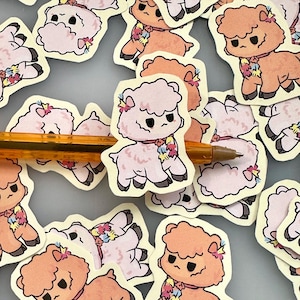 Könnte beinhalten: Eine Ansammlung von Aufklebern mit Cartoon-Alpakas. Die Aufkleber sind in Rosa- und Orangetönen gehalten und haben schwarze Umrisse und florale Akzente. Die Alpakas haben einen leicht mürrischen Gesichtsausdruck. Ein Stift ist ebenfalls sichtbar.
