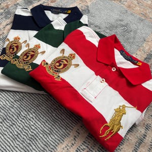 Puede incluir: Tres polos plegados a rayas azul marino y blanco, verde y blanco, y rojo y blanco. Cada camisa tiene un cuello en contraste y logotipos bordados. La camisa roja y blanca presenta un logotipo ecuestre dorado.