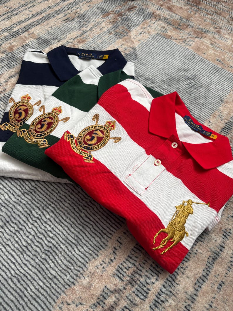 Puede incluir: Tres polos plegados a rayas azul marino y blanco, verde y blanco, y rojo y blanco. Cada camisa tiene un cuello en contraste y logotipos bordados. La camisa roja y blanca presenta un logotipo ecuestre dorado.