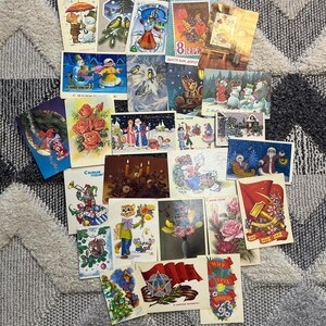 May include: A collection of vintage postcards featuring various illustrations and designs. Some postcards depict winter scenes, others feature flowers, and some have a patriotic theme. The postcards are in various colors and styles.
