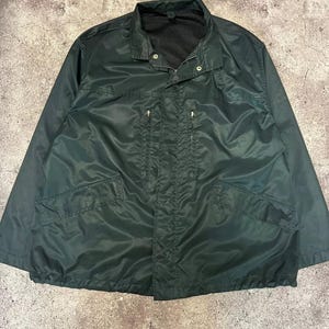 Könnte beinhalten: Eine dunkelgrüne, leichte Jacke mit Reißverschluss und mehreren Taschen. Die Jacke hat ein Mesh-Futter und einen Kordelzug in der Taille.