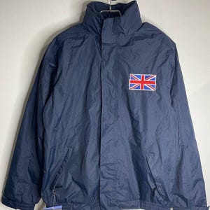 May include: A navy blue jacket with a zip fastening and a small Union Jack flag patch on the chest. The jacket has a high collar and a drawstring at the waist.