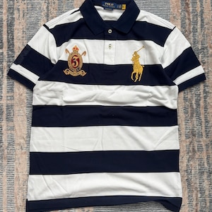 Puede incluir: Polo a rayas azul marino y blanco con mangas cortas. La camisa tiene cuello azul marino y tapeta de tres botones. Cuenta con un logotipo ecuestre dorado y un escudo con el n&uacute;mero 6 bordado en el pecho.