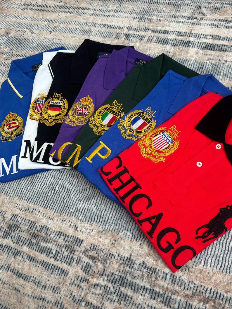 May include: A collection of polo shirts in various colors, including blue, white, black, purple, green, and red. Each shirt features embroidered crests and the word "CHICAGO" on the red shirt.