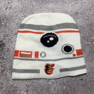 May include: White knitted beanie with a black and white design of a robot's face. The beanie has orange and grey stripes and a small orange and black Baltimore Orioles logo on the front.