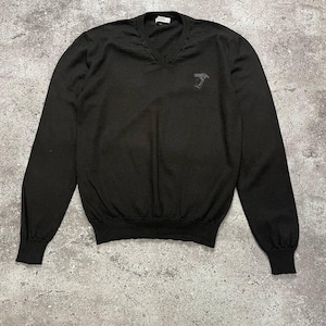 Puede incluir: Jersey negro de manga larga y cuello en V con un pequeño logotipo bordado en el pecho. El logotipo es una imagen en blanco y negro de una cabeza con una corona.