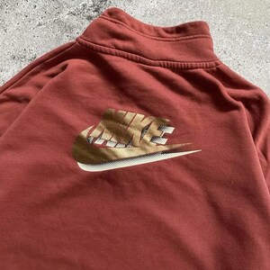 May include: A red sweatshirt with a gold Nike logo on the front. The logo is a stylized swoosh with the word "NIKE" written in a bold font.