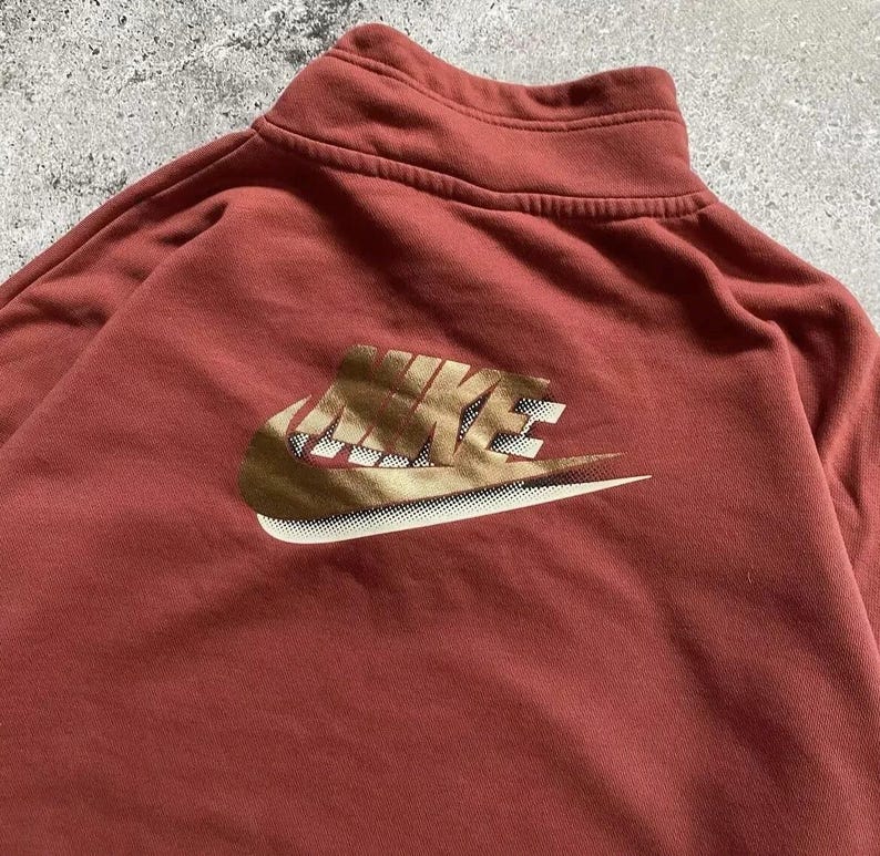May include: A red sweatshirt with a gold Nike logo on the front. The logo is a stylized swoosh with the word "NIKE" written in a bold font.