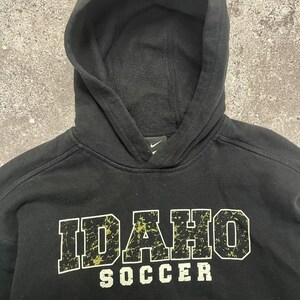 May include: Black hooded sweatshirt with a distressed white and yellow graphic that says "IDAHO SOCCER".