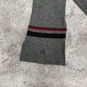May include: Gray sweater with a red and black striped cuff and a small embroidered logo.