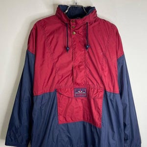 May include: A red and blue windbreaker jacket with a drawstring hood and a zip closure. The jacket has a large pocket on the front and a small logo patch on the left chest. The logo says "Sun Ice".