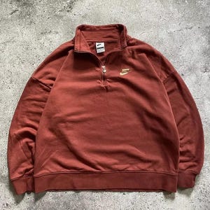 May include: A rust-colored quarter-zip sweatshirt with a gold Nike logo on the chest.