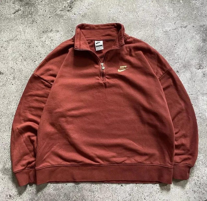 May include: A rust-colored quarter-zip sweatshirt with a gold Nike logo on the chest.