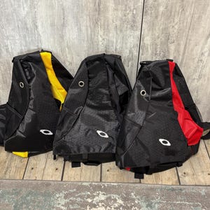 Może przedstawiać: Trzy czarne plecaki typu sling z teksturowanym wzorem. Jeden ma żółty akcent, drugi czerwony, a trzeci jest cały czarny. Każda torba ma białe logo i metalową przelotkę.