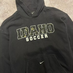 May include: Black hooded sweatshirt with the text "IDAHO SOCCER" in yellow and white lettering. The Nike logo is on the front and back of the sweatshirt.