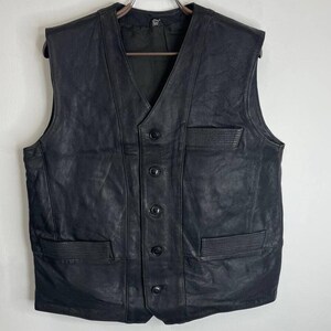Könnte beinhalten: Eine schwarze Lederweste mit Knopfleiste und zwei Taschen. Die Weste hat einen V-Ausschnitt und eine glatte Lederoberfläche.