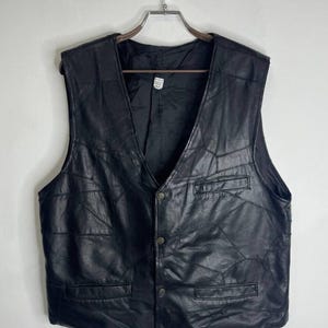 Könnte beinhalten: Eine schwarze Lederweste mit Knopfleiste und mehreren Taschen. Die Weste ist aus einem Patchwork aus Lederstücken gefertigt.