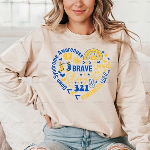 May include: A beige sweatshirt with a blue and yellow heart design. The heart includes the words "Down Syndrome Awareness", "Brave", "Strong", "Loved", "Kindness", and "321".