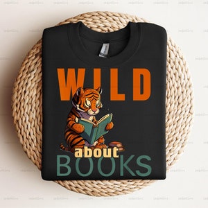 Pu&ograve; includere: Maglietta nera con una tigre di cartone animato che legge un libro. Il testo "WILD about BOOKS" &egrave; stampato sulla maglietta.