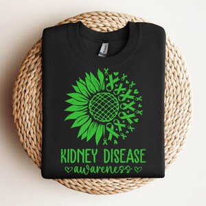 May include: Black t-shirt with a green sunflower design made of awareness ribbons. The text "Kidney Disease Awareness" is printed below the sunflower.