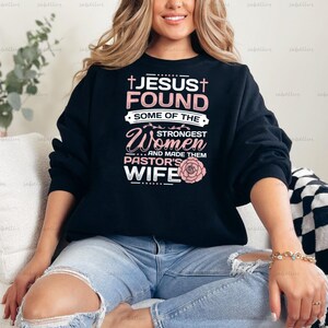 May include: Black sweatshirt with a pink and white design that says "Jesus Found Some of the Strongest Women and Made Them Pastor's Wife".