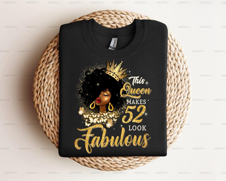 May include: Black t-shirt with a gold crown and a black woman with gold jewelry. The text on the shirt reads "This Queen Makes 52 Look Fabulous".