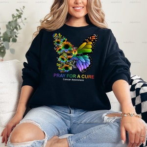 May include: Black sweatshirt with a colorful butterfly and flower design. The text "Pray for a Cure" and "Cancer Awareness" is printed on the front of the sweatshirt.