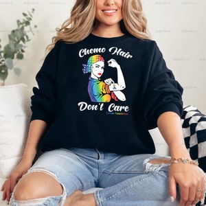 May include: Black sweatshirt with a rainbow-colored graphic of a woman with a headscarf and the text "Chemo Hair Don't Care Cancer Awareness".