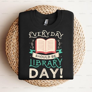 Pu&ograve; includere: Maglietta nera con un design bianco e verde che dice "EVERYDAY SHOULD BE LIBRARY DAY!" con un'illustrazione di un libro aperto.
