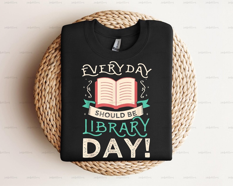Pu&ograve; includere: Maglietta nera con un design bianco e verde che dice "EVERYDAY SHOULD BE LIBRARY DAY!" con un'illustrazione di un libro aperto.