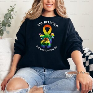 May include: A black sweatshirt with a rainbow ribbon and the text "She Believed She Could, So She Did".