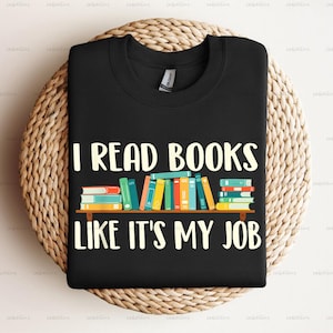 Pu&ograve; includere: Maglietta nera con il testo "I read books like it's my job" in bianco. Sopra il testo &egrave; raffigurata una pila di libri colorati.