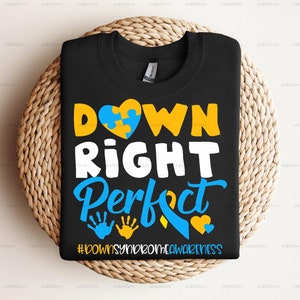 May include: Black t-shirt with a yellow and blue puzzle piece heart, the words "DOWN RIGHT PERFECT" in white, and the hashtag "#DOWNSYNROMEAWARENESS" in white.