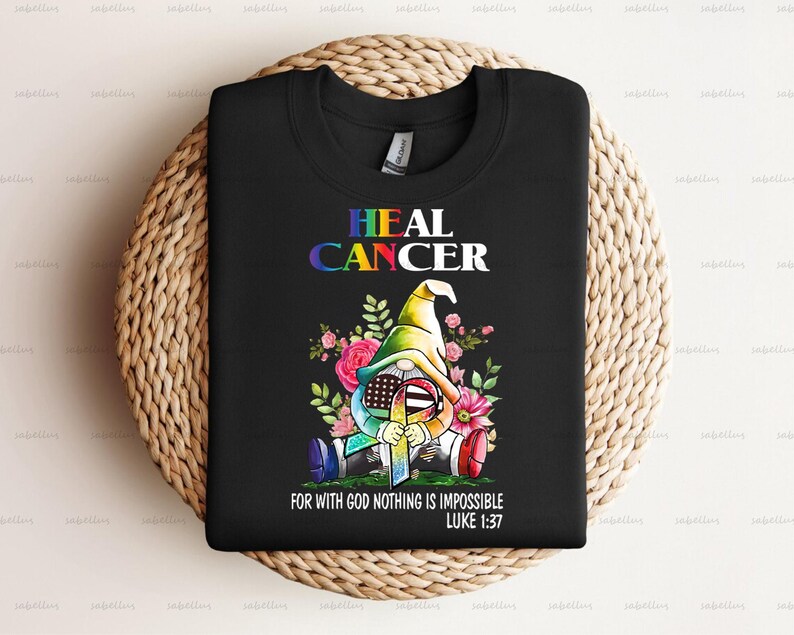 May include: Black t-shirt with a colorful graphic of a gnome wearing a rainbow hat and holding a ribbon. The text "HEAL CANCER" is above the gnome and the text "FOR WITH GOD NOTHING IS IMPOSSIBLE LUKE 1:37" is below the gnome.