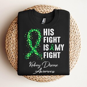 May include: Black t-shirt with a green ribbon design and the text "His Fight Is My Fight Kidney Disease Awareness".