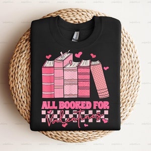 Pu&ograve; includere: Maglietta nera con una grafica rosa e bianca di libri impilati con cuori e il testo "All Booked For Valentines".