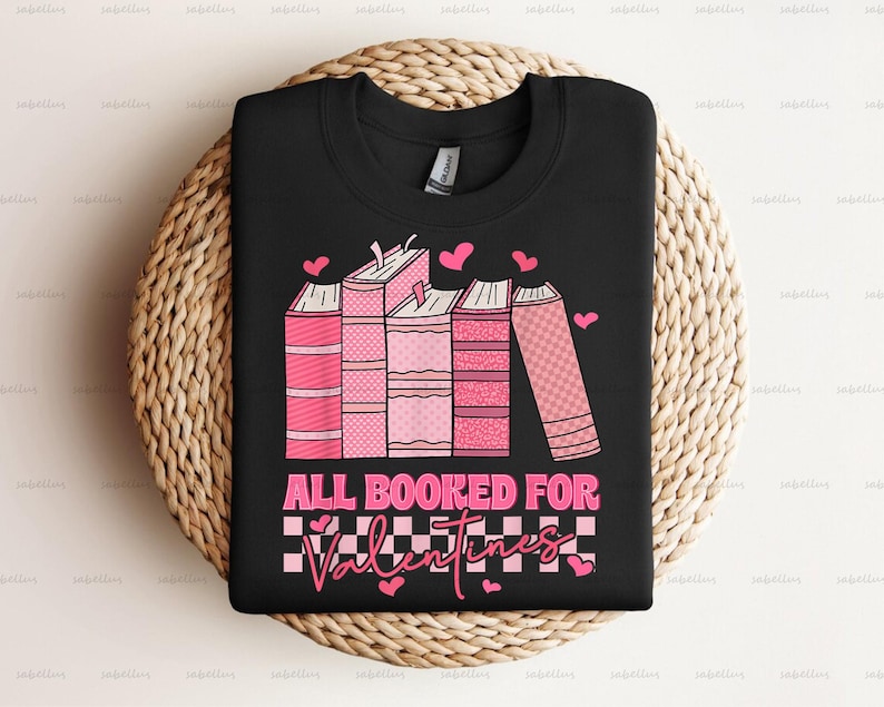Pu&ograve; includere: Maglietta nera con una grafica rosa e bianca di libri impilati con cuori e il testo "All Booked For Valentines".