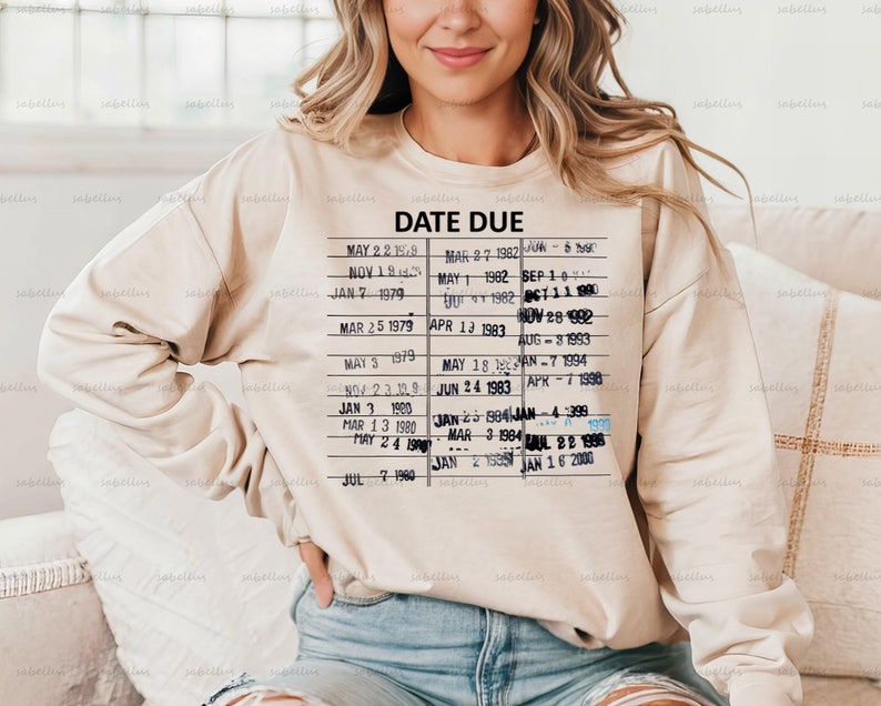 Pu&ograve; includere: Una felpa beige con un design di carta di biblioteca vintage che presenta il testo "DATE DUE" e un elenco di date da maggio 1979 a gennaio 2000.