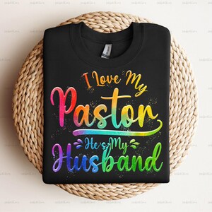 May include: Black t-shirt with a rainbow design that says "I Love My Paston He's My Husband".