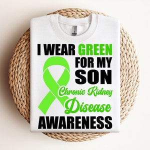 May include: White t-shirt with a green ribbon and the text "I wear green for my son Chronic Kidney Disease Awareness".